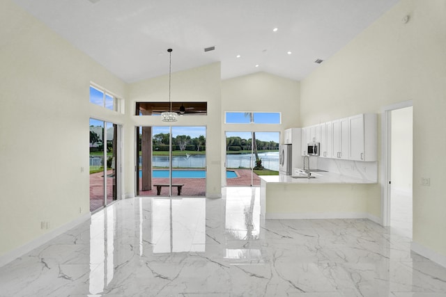 interior space featuring kitchen peninsula, pendant lighting, a water view, high vaulted ceiling, and white cabinets