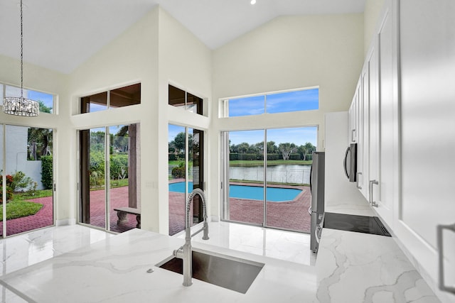 interior space with a notable chandelier, a water view, sink, and high vaulted ceiling