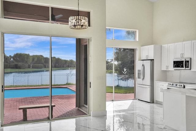 interior space featuring a water view, appliances with stainless steel finishes, decorative light fixtures, white cabinetry, and a chandelier