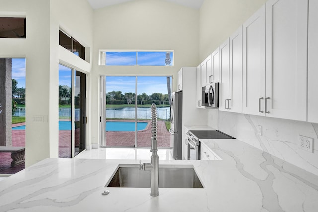 kitchen featuring a water view, sink, light stone countertops, appliances with stainless steel finishes, and white cabinetry