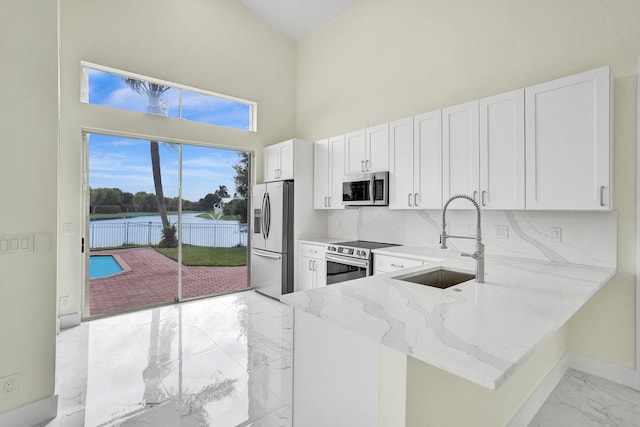 kitchen featuring kitchen peninsula, light stone counters, white cabinets, and appliances with stainless steel finishes