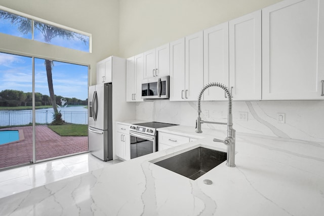 kitchen with light stone countertops, sink, white cabinets, a water view, and appliances with stainless steel finishes