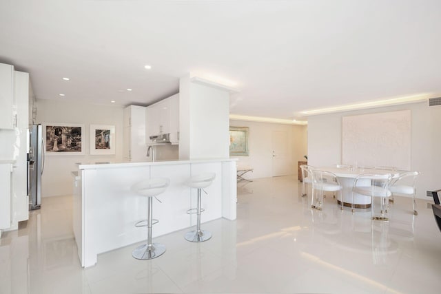 kitchen featuring light tile patterned flooring, a kitchen bar, stainless steel refrigerator, white cabinets, and kitchen peninsula