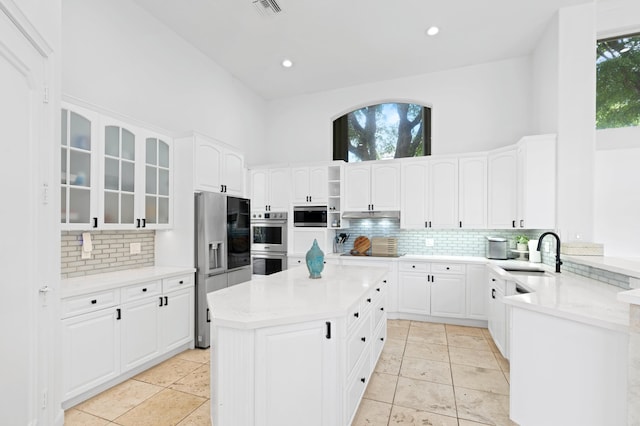 kitchen with stainless steel appliances, sink, light tile patterned floors, white cabinetry, and a kitchen island