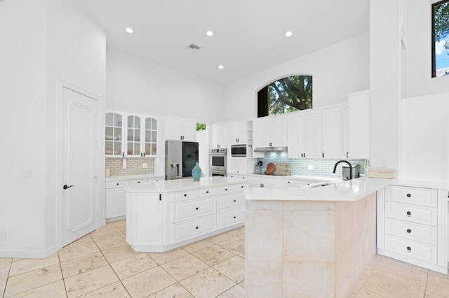 kitchen featuring a high ceiling, white cabinets, kitchen peninsula, a kitchen island, and appliances with stainless steel finishes