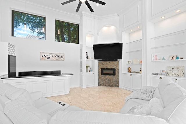 tiled living room with ceiling fan, a fireplace, and ornamental molding