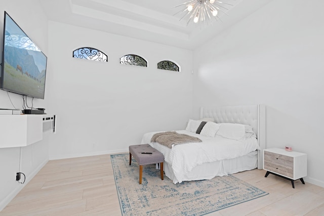 bedroom with ceiling fan with notable chandelier, light hardwood / wood-style floors, and a raised ceiling