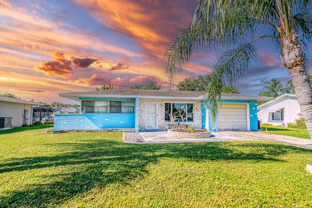 ranch-style house featuring a lawn, central AC unit, and a garage