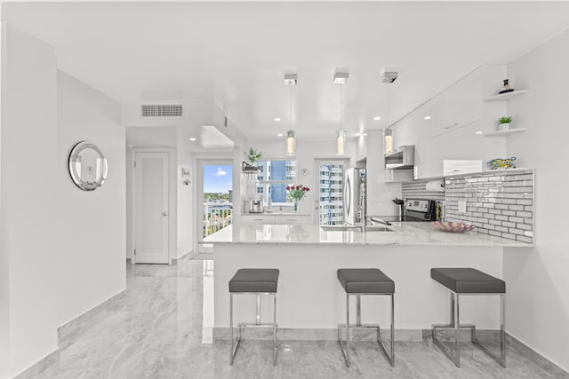 kitchen with a kitchen bar, appliances with stainless steel finishes, kitchen peninsula, pendant lighting, and white cabinets