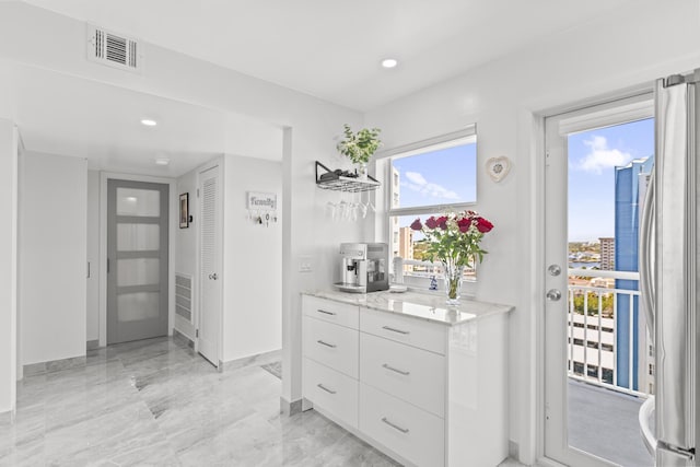 interior space with stainless steel refrigerator, white cabinetry, and light stone countertops