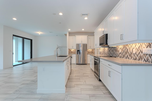 kitchen with decorative backsplash, stainless steel appliances, sink, a center island with sink, and white cabinets