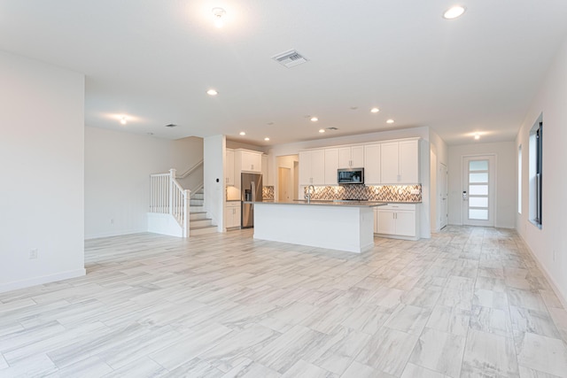 kitchen featuring a center island with sink, backsplash, white cabinetry, and stainless steel appliances