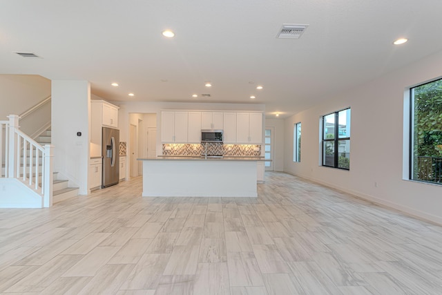 kitchen featuring decorative backsplash, white cabinetry, a center island with sink, and appliances with stainless steel finishes