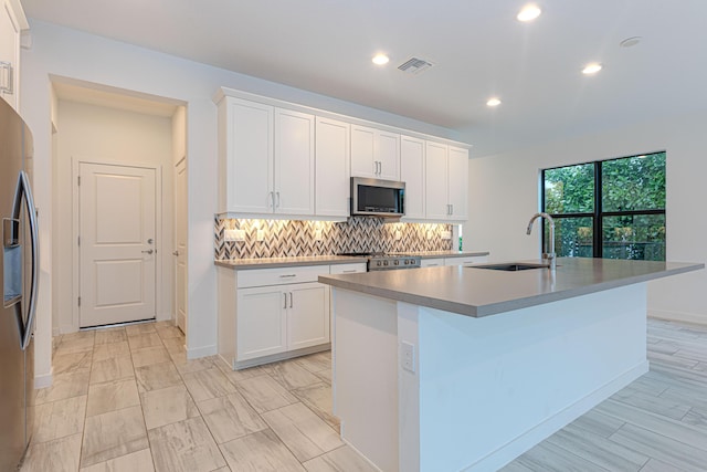 kitchen featuring a kitchen island with sink, white cabinets, sink, decorative backsplash, and appliances with stainless steel finishes