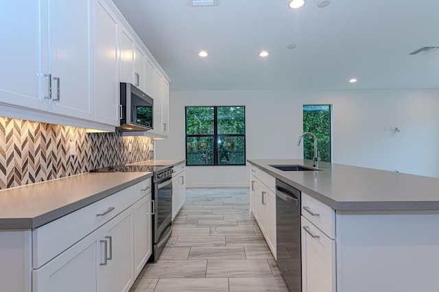 kitchen featuring backsplash, sink, an island with sink, appliances with stainless steel finishes, and white cabinetry