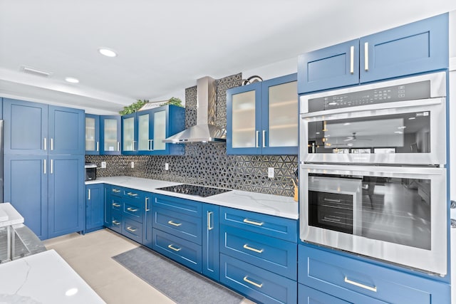 kitchen with black electric stovetop, light stone counters, wall chimney exhaust hood, backsplash, and double oven