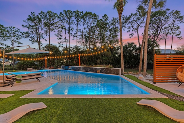 pool at dusk with a hot tub, a lawn, and a patio