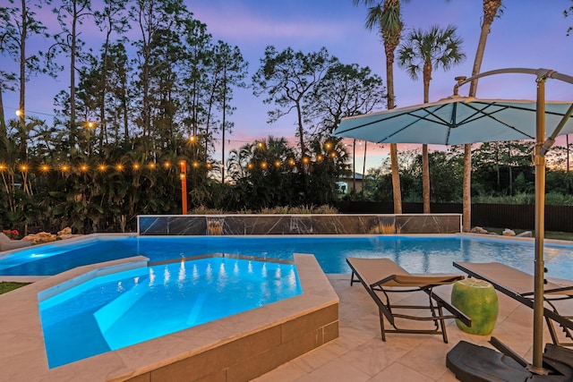 pool at dusk featuring a jacuzzi and a patio area