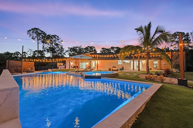 pool at dusk featuring a lawn, an in ground hot tub, and a patio area