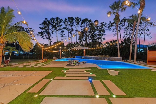 pool at dusk with a patio and a lawn