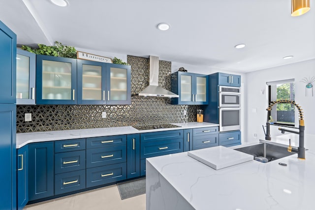 kitchen with stainless steel double oven, wall chimney exhaust hood, blue cabinetry, and tasteful backsplash