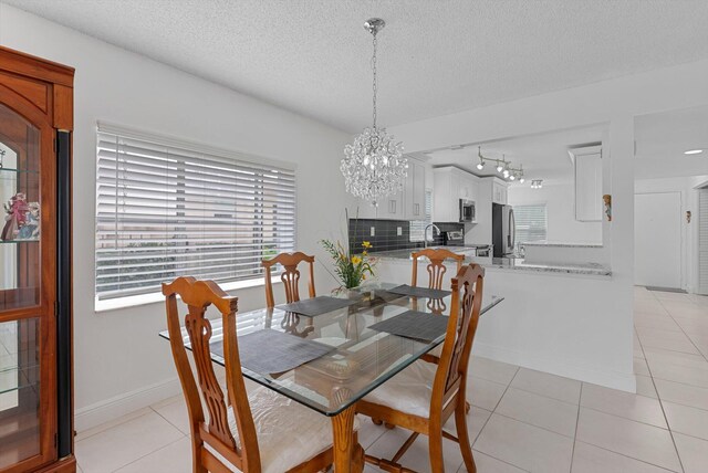 dining space featuring an inviting chandelier, rail lighting, a textured ceiling, and light tile patterned flooring