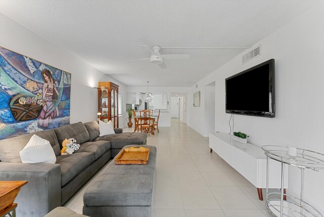 tiled living room featuring ceiling fan with notable chandelier and a textured ceiling