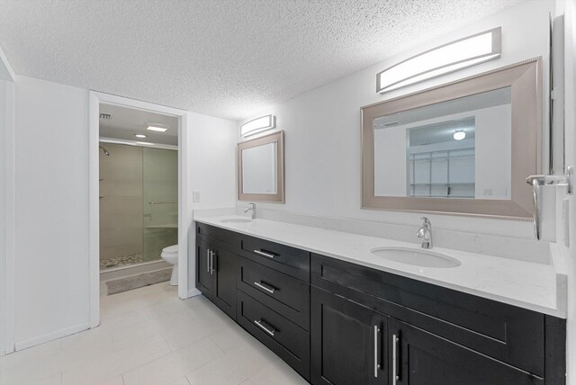 bathroom featuring toilet, vanity, a textured ceiling, and a shower with shower door