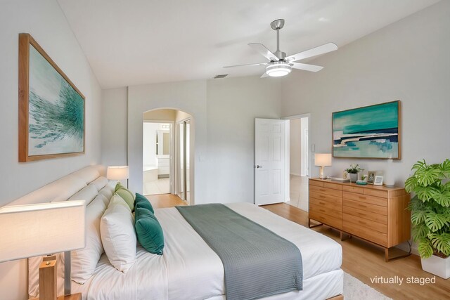 bedroom featuring arched walkways, lofted ceiling, light wood-style floors, ensuite bathroom, and a ceiling fan