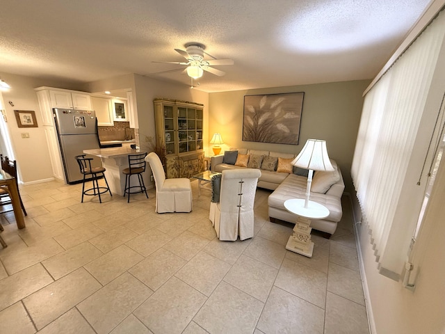 living room featuring a textured ceiling, ceiling fan, sink, and light tile patterned floors