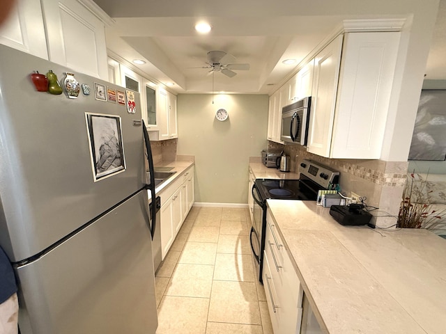 kitchen with a tray ceiling, white cabinetry, appliances with stainless steel finishes, and decorative backsplash