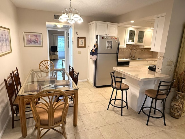 kitchen featuring white cabinetry, stainless steel refrigerator, a notable chandelier, sink, and kitchen peninsula