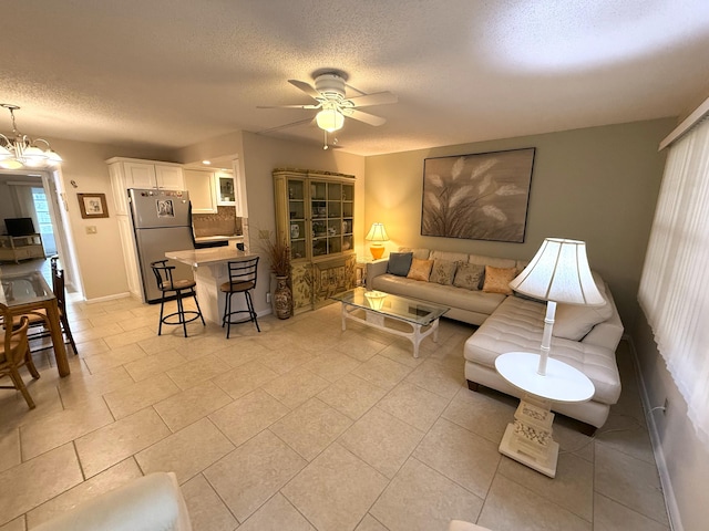 tiled living room featuring ceiling fan with notable chandelier and a textured ceiling