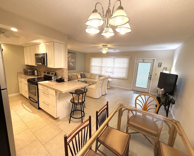 kitchen featuring tasteful backsplash, stainless steel appliances, decorative light fixtures, white cabinets, and ceiling fan with notable chandelier