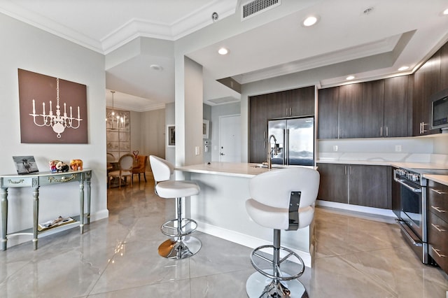 kitchen featuring appliances with stainless steel finishes, a kitchen breakfast bar, ornamental molding, a notable chandelier, and an island with sink