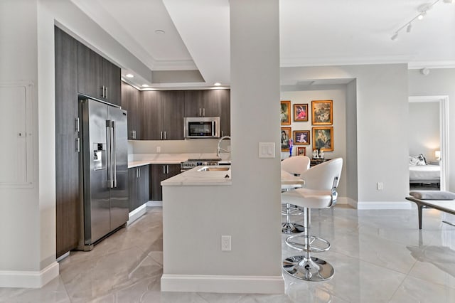 kitchen featuring appliances with stainless steel finishes, ornamental molding, dark brown cabinets, sink, and a breakfast bar area