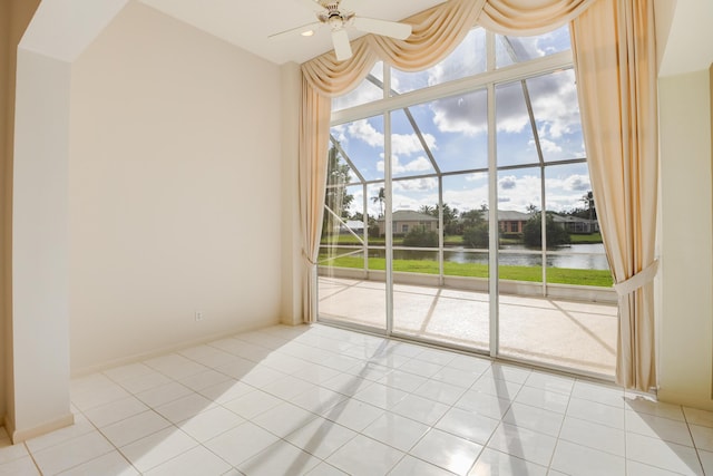 tiled empty room with ceiling fan, expansive windows, and a water view