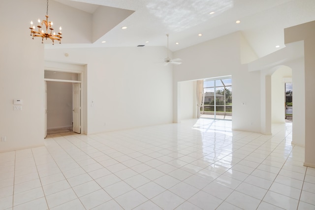 empty room featuring light tile patterned floors, ceiling fan with notable chandelier, and a high ceiling