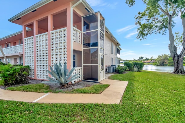 1260 NW 20th Ave Unit 203, Delray Beach, FL 33445 - view of side of property featuring central air condition unit, a sunroom, a lawn, stucco siding, and a water view