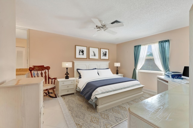 bedroom featuring ceiling fan, light tile patterned floors, and a textured ceiling