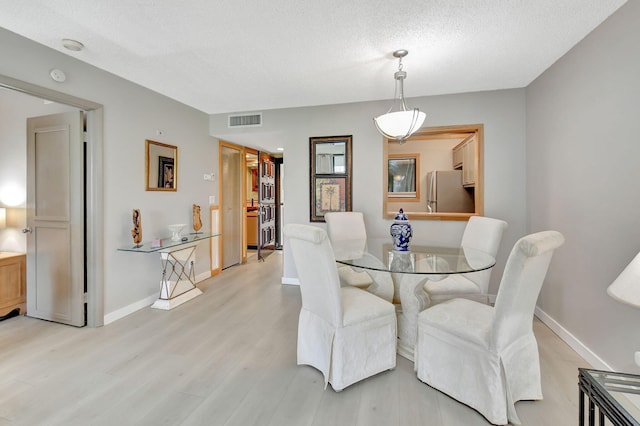 dining space with a textured ceiling and light hardwood / wood-style flooring