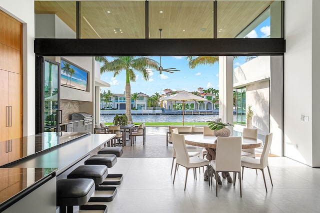 dining area with a high ceiling, ceiling fan, a water view, and a healthy amount of sunlight