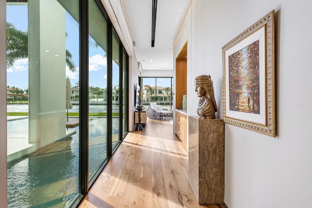 hallway with expansive windows, a water view, and light hardwood / wood-style floors