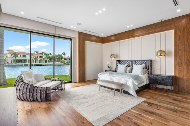 bedroom with hardwood / wood-style floors, access to outside, and a water view