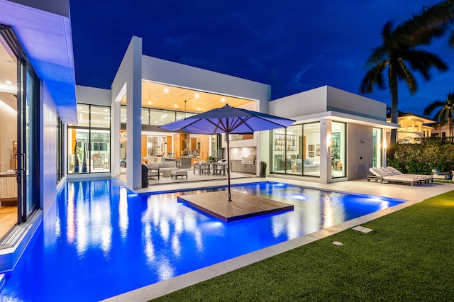 pool at twilight with outdoor lounge area, a lawn, and a patio