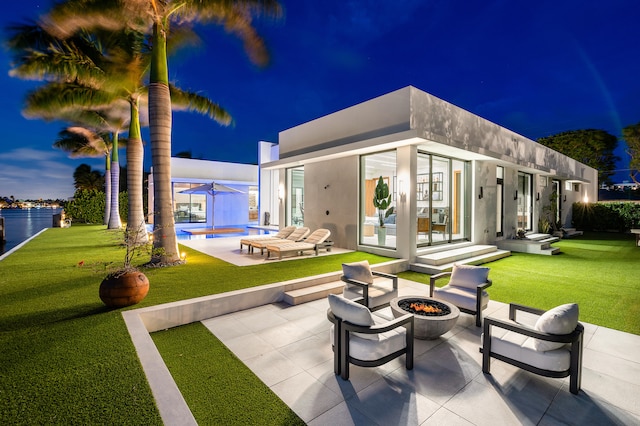 rear view of property featuring a patio, a lawn, an outdoor fire pit, and a water view