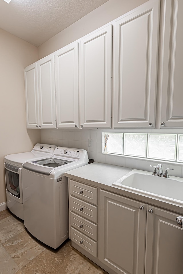 clothes washing area featuring sink, washing machine and dryer, cabinets, and a textured ceiling