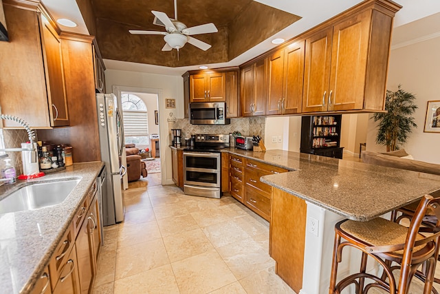 kitchen with appliances with stainless steel finishes, stone countertops, sink, a breakfast bar area, and kitchen peninsula