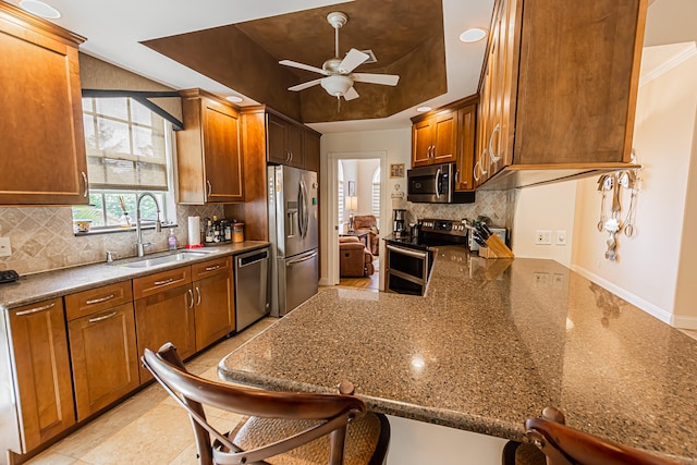 kitchen featuring sink, a breakfast bar area, appliances with stainless steel finishes, a tray ceiling, and kitchen peninsula