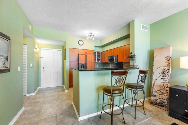 kitchen featuring fridge with ice dispenser, a textured ceiling, light tile patterned floors, a breakfast bar area, and kitchen peninsula